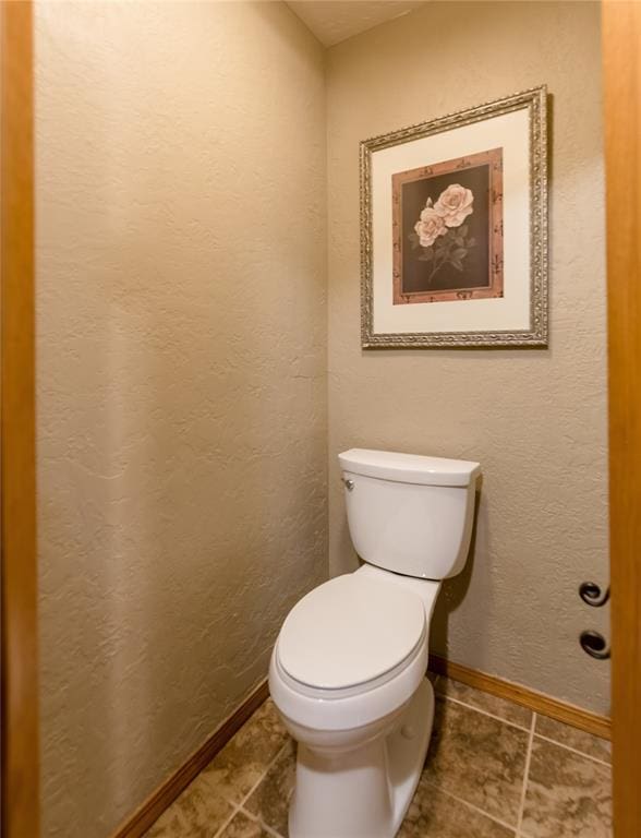 bathroom featuring toilet, baseboards, and a textured wall