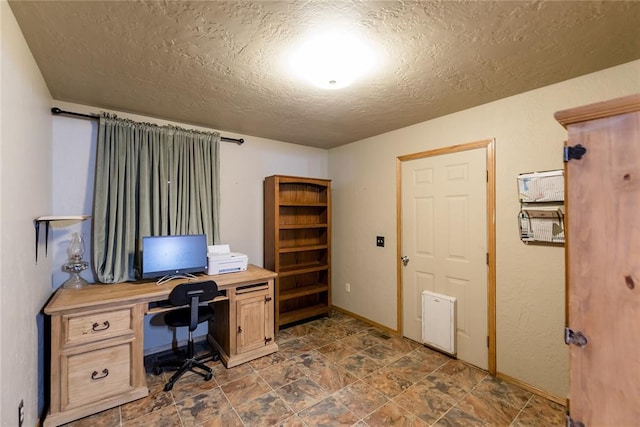 home office featuring a textured ceiling, stone finish flooring, and baseboards