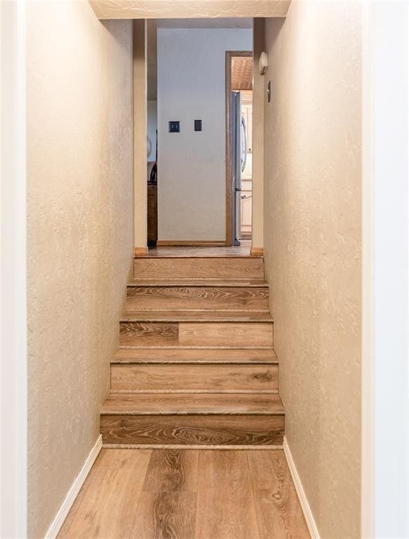 stairway with a textured wall, wood finished floors, and baseboards