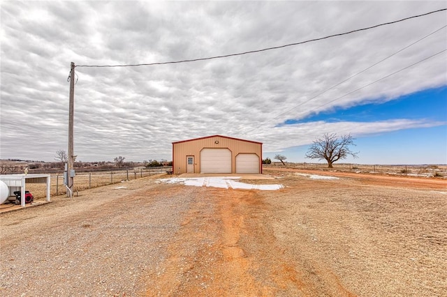 exterior space featuring driveway, fence, an outdoor structure, and a rural view