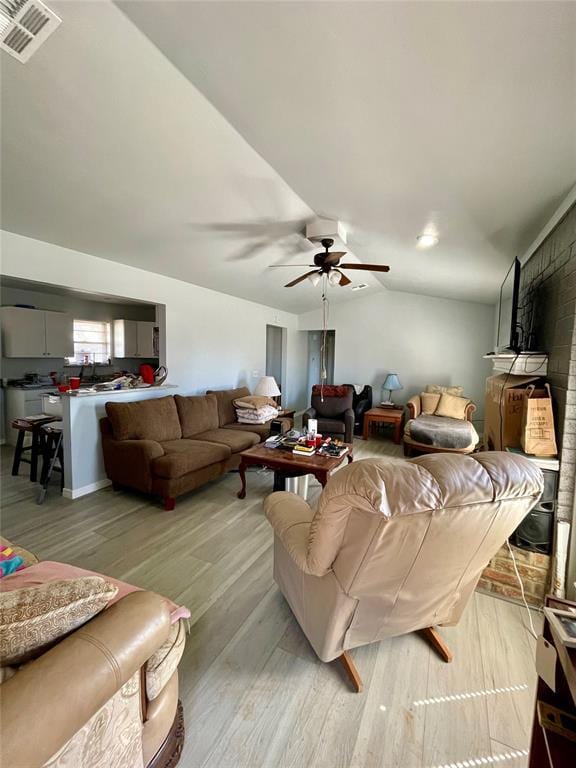 living room with lofted ceiling, light wood-style flooring, visible vents, and a ceiling fan