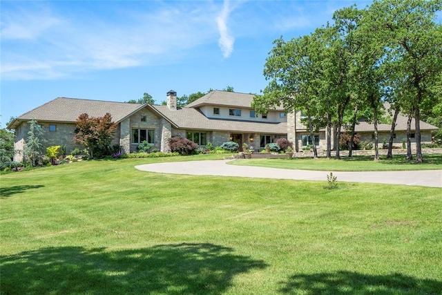 view of front of home featuring driveway, a front lawn, a chimney, and stone siding