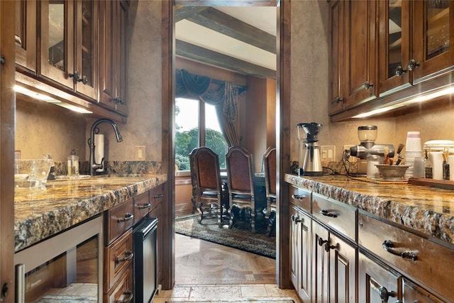 kitchen with stone countertops, wine cooler, glass insert cabinets, dark brown cabinets, and a sink