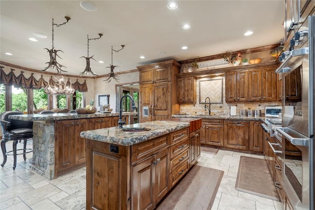 kitchen featuring pendant lighting, stone tile floors, stone countertops, a kitchen island with sink, and a sink