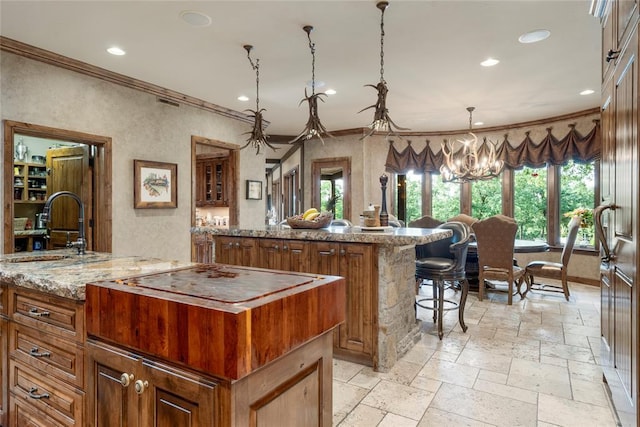 kitchen featuring a center island, brown cabinets, decorative light fixtures, stone tile flooring, and a sink