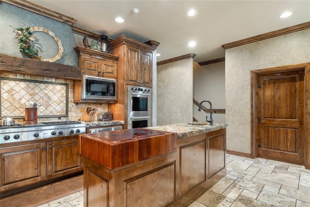 kitchen with stone tile floors, an island with sink, appliances with stainless steel finishes, crown molding, and a sink