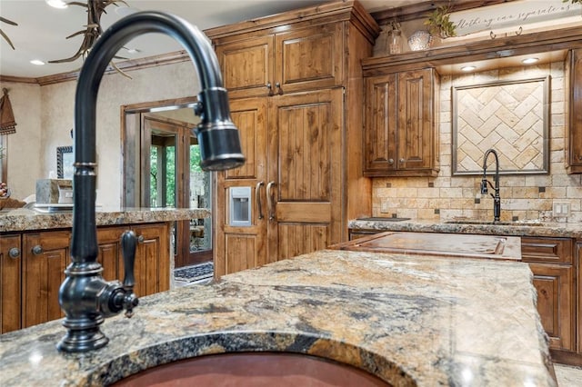 kitchen featuring crown molding, brown cabinetry, decorative backsplash, and light stone countertops