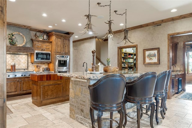 kitchen with appliances with stainless steel finishes, a kitchen island with sink, crown molding, and stone tile floors