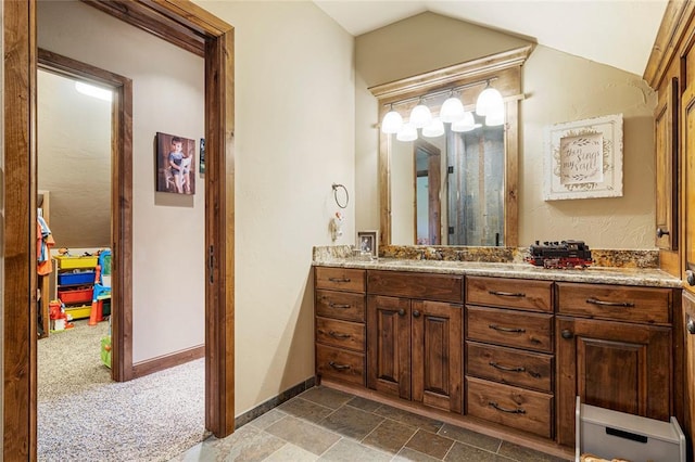 bathroom featuring stone finish flooring, vaulted ceiling, vanity, and baseboards