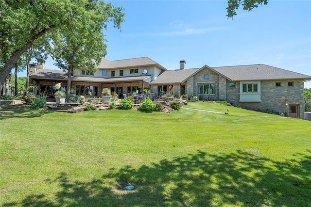 back of property featuring a yard, a chimney, and stone siding