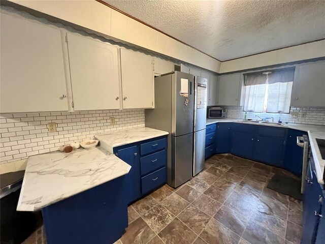 707 S Third St, Cheyenne, OK 73628 - kitchen featuring appliances with stainless steel finishes, a textured ceiling, tasteful backsplash, a sink, and blue cabinets