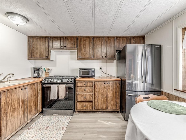 kitchen with light wood-style flooring, brown cabinets, stainless steel appliances, light countertops, and a sink