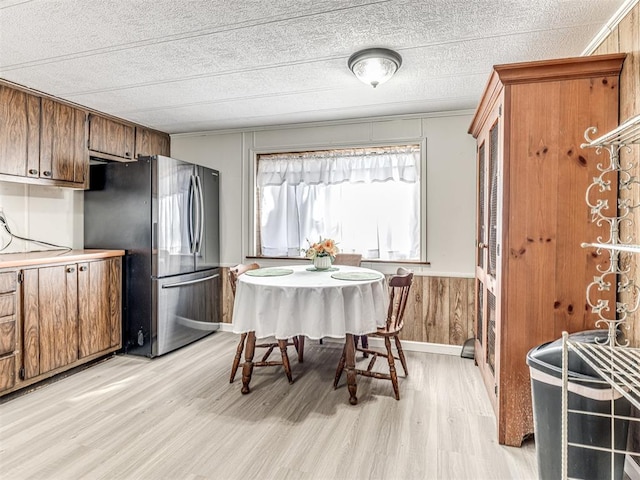 kitchen featuring a wainscoted wall, wood walls, freestanding refrigerator, brown cabinets, and light wood finished floors