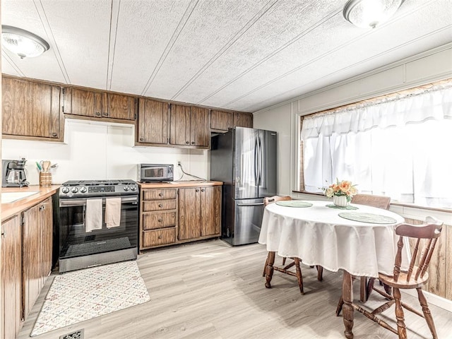 kitchen with light wood finished floors, brown cabinets, stainless steel appliances, a textured ceiling, and light countertops