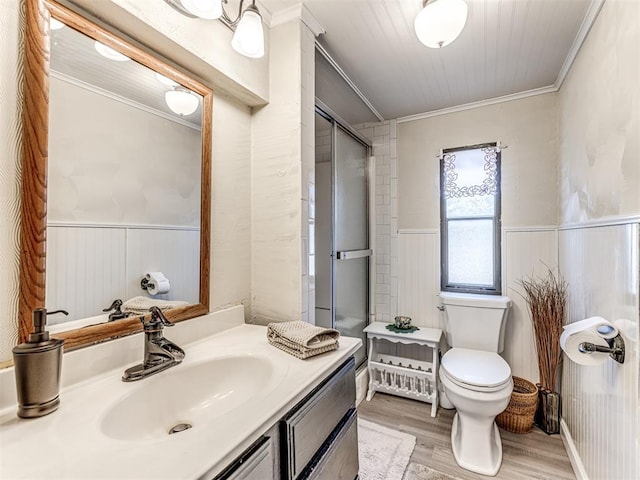 bathroom featuring a wainscoted wall, a shower with door, toilet, ornamental molding, and wood finished floors