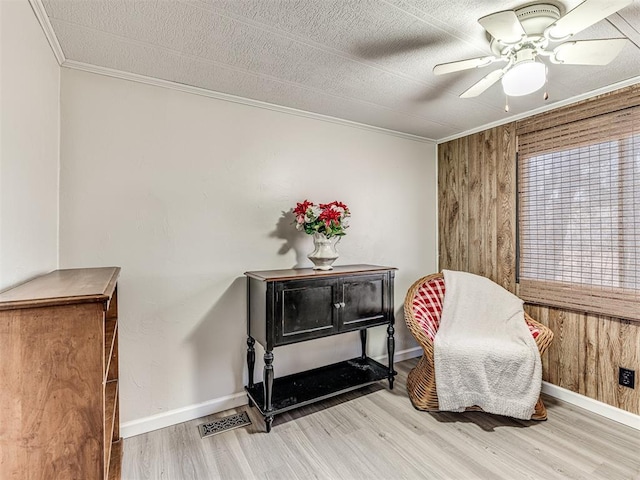 living area featuring baseboards, visible vents, a ceiling fan, wood finished floors, and crown molding