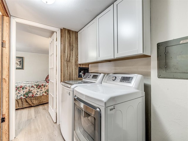 laundry room featuring light wood-style flooring, washer and clothes dryer, cabinet space, and electric panel