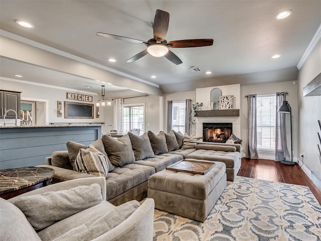 living room with ornamental molding, a wealth of natural light, dark wood-type flooring, and a lit fireplace