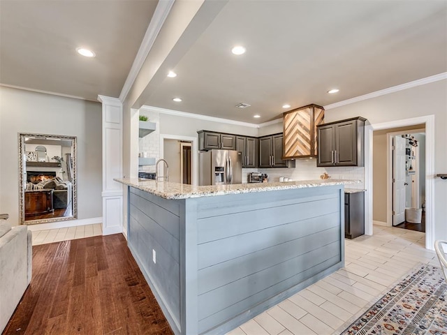 kitchen featuring light stone counters, a peninsula, gray cabinets, stainless steel fridge, and crown molding