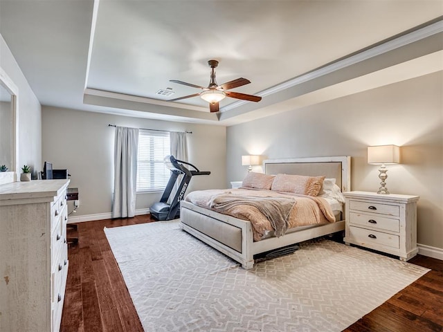 bedroom with visible vents, a tray ceiling, dark wood finished floors, and baseboards