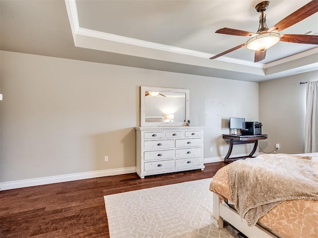 bedroom with dark wood-type flooring, a ceiling fan, baseboards, ornamental molding, and a raised ceiling