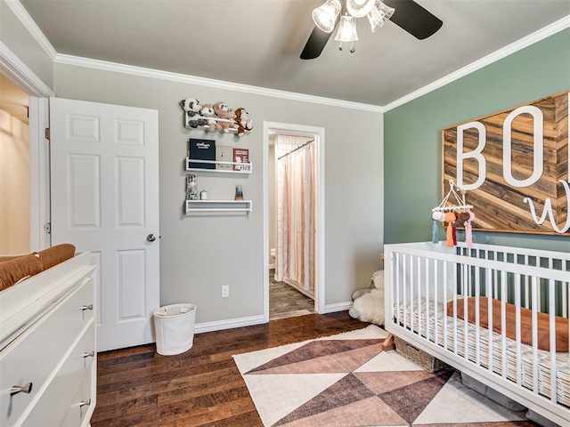 bedroom featuring dark wood-style floors, crown molding, ceiling fan, a crib, and baseboards