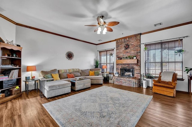 living room featuring a brick fireplace, crown molding, visible vents, and wood finished floors