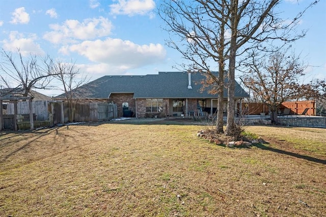 rear view of property with brick siding, a lawn, and fence