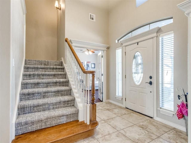 foyer entrance featuring light tile patterned floors, visible vents, a towering ceiling, baseboards, and stairs