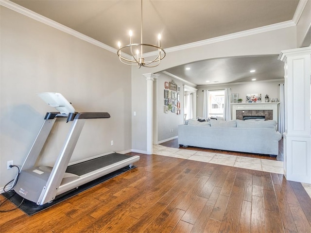 exercise room with arched walkways, crown molding, a fireplace, decorative columns, and light wood-style flooring