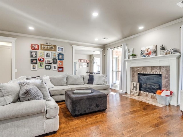 living area featuring ornamental molding, a tiled fireplace, and wood finished floors