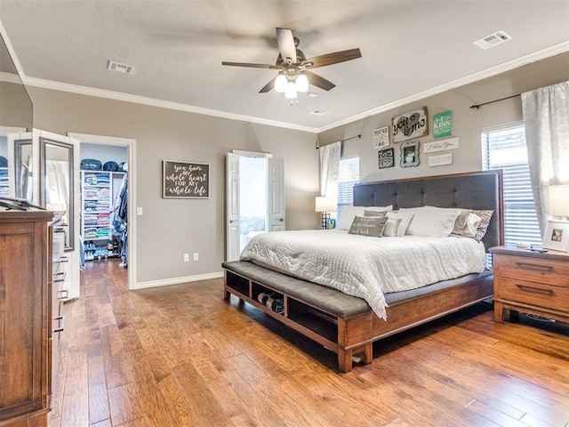 bedroom with a walk in closet, visible vents, ornamental molding, wood finished floors, and baseboards