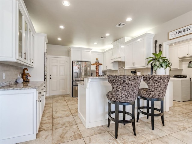 kitchen featuring light stone counters, white cabinets, stainless steel fridge with ice dispenser, washer / clothes dryer, and glass insert cabinets