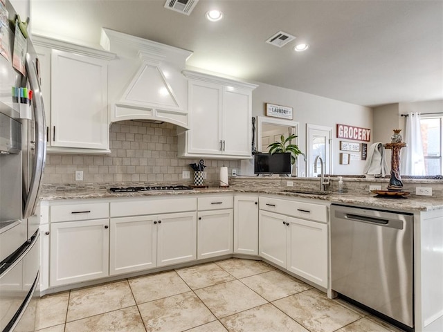 kitchen with appliances with stainless steel finishes, white cabinetry, a sink, and light stone countertops