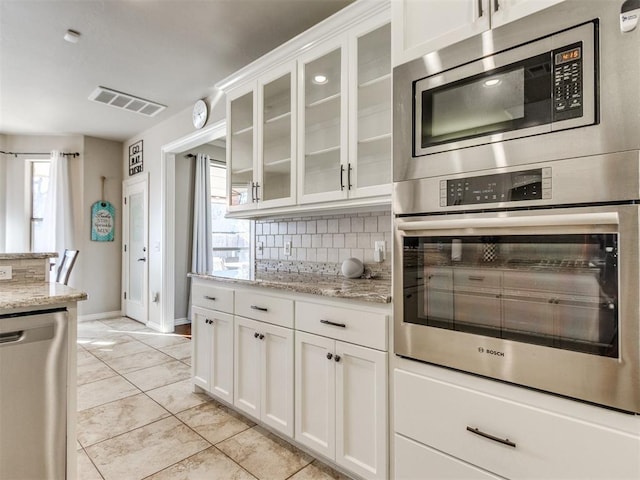 kitchen featuring light stone counters, stainless steel appliances, visible vents, glass insert cabinets, and white cabinetry