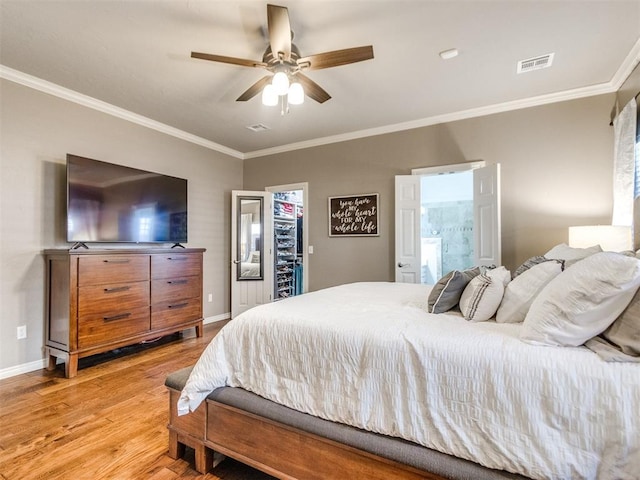 bedroom with a walk in closet, light wood finished floors, visible vents, ornamental molding, and baseboards