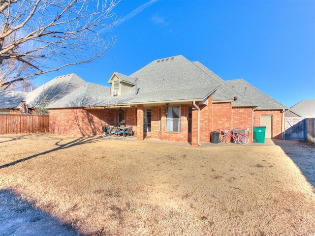 back of property featuring brick siding, a patio, a fenced backyard, and roof with shingles