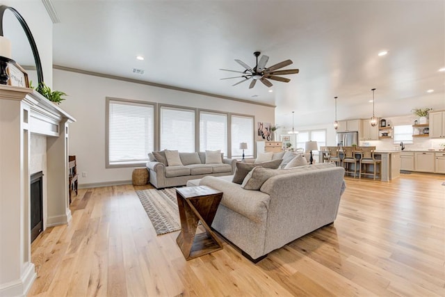 living room with a ceiling fan, a fireplace, crown molding, and light wood finished floors