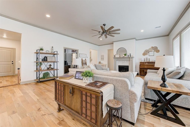 living room featuring visible vents, ceiling fan, ornamental molding, light wood-type flooring, and a fireplace