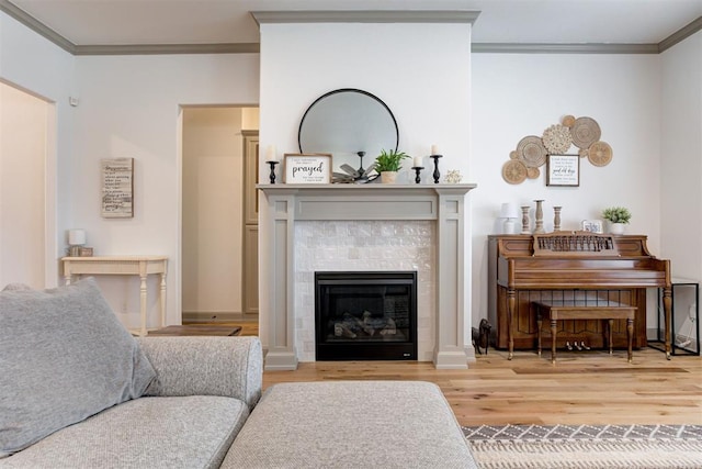 living area with a tiled fireplace, ornamental molding, and wood finished floors