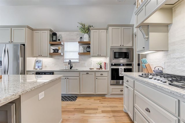 kitchen with light wood finished floors, tasteful backsplash, appliances with stainless steel finishes, open shelves, and a sink