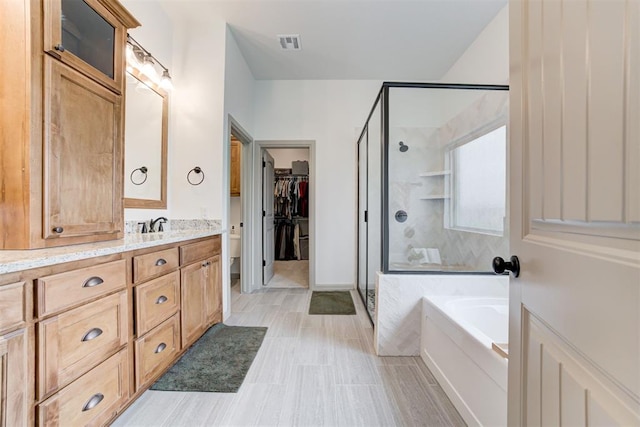 bathroom featuring a stall shower, visible vents, a walk in closet, vanity, and a bath