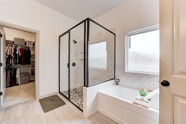 bathroom with a spacious closet, a stall shower, and a garden tub