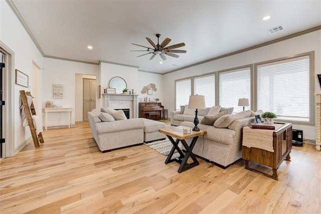 living area with visible vents, ornamental molding, ceiling fan, a fireplace, and light wood-style flooring