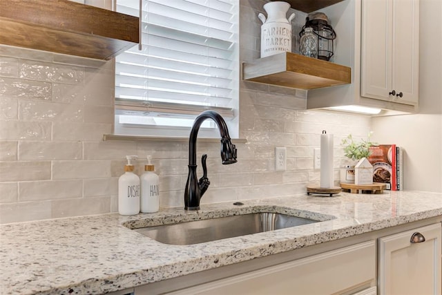 interior details with a sink, decorative backsplash, open shelves, and light stone countertops