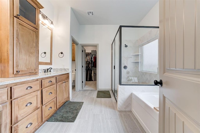 full bath featuring a garden tub, vanity, visible vents, a walk in closet, and a stall shower