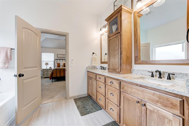 ensuite bathroom with double vanity, a sink, a tub to relax in, and connected bathroom