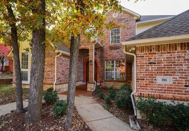 entrance to property with brick siding and a shingled roof