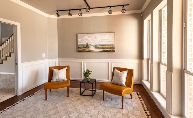 living area with crown molding, stairway, a decorative wall, and wood finished floors