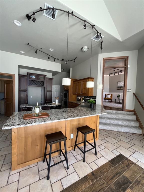 kitchen with visible vents, lofted ceiling, dark stone countertops, decorative light fixtures, and a peninsula